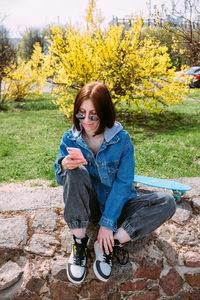 Young stylish woman walks on street with a skateboard and uses a smartphone