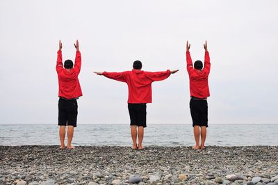 Rear view of friends exercising at beach against sky