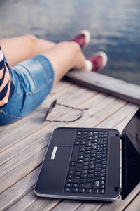 Low section of woman sitting by laptop on pier