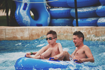 Happy father with son siting on inflatable raft in pool