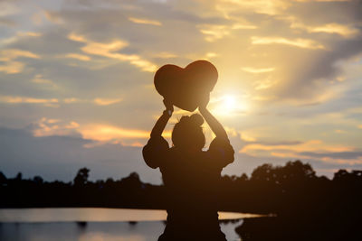 Silhouette woman with arms raised standing against sky during sunset