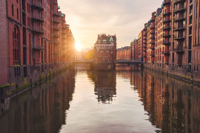 Canal amidst buildings in city against sky during sunset