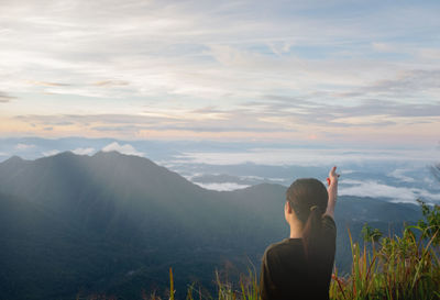 Rear view of woman pointing at mountain against sky during sunset