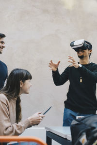 Smiling male computer programmer gesturing while using vr glasses by colleagues in office