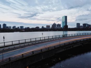 Bridge over river by buildings in city against sky