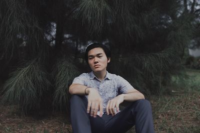 Thoughtful young man looking away while sitting against trees