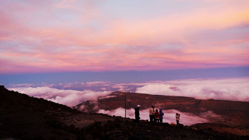People standing on mountain against cloudy sky during sunset