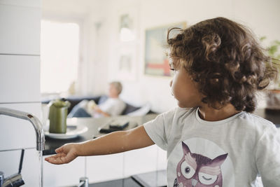 Girl looking away while washing hand under faucet at home