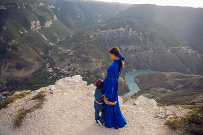 Mother in a blue dress with her son stands on the cliff of the sulak canyon in dagestan