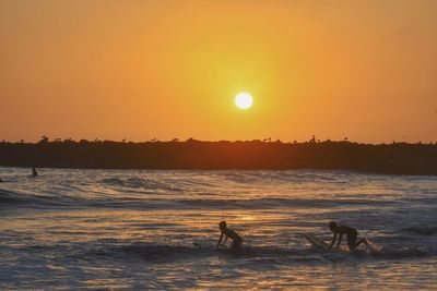 Silhouette people on beach against sky during sunset