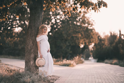 Pregnant woman leaning on tree at park during sunset