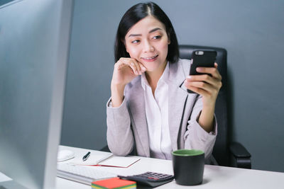 Portrait of a smiling young woman using mobile phone while sitting on table