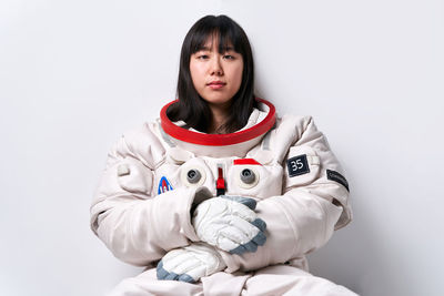 Serious young asian female in spacesuit looking at camera while sitting near gray wall during space mission