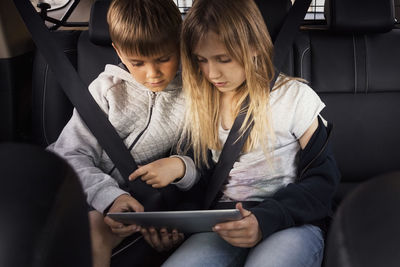 Sibling using digital tablet while sitting in electric car