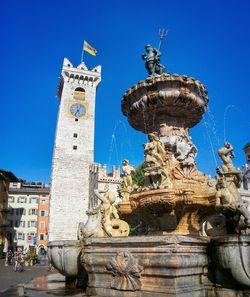 Low angle view of fountain and clock tower against clear blue sky