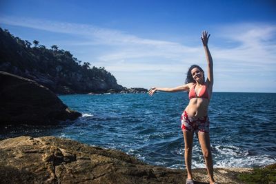 Woman standing on rock by sea against sky