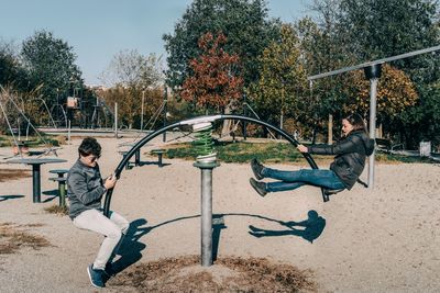 Side view of friends sitting on seesaw at playground