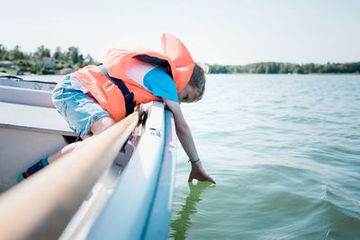 Young boy dipping his hands in the water whilst on a boat in summer