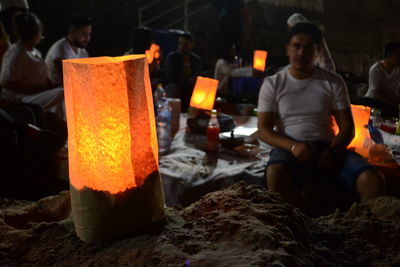 Friends with illuminated lanterns camping on beach at night