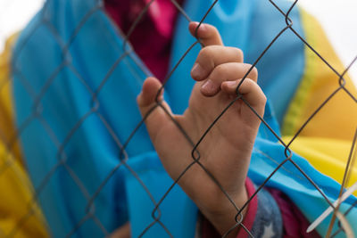 A little refugee girl with a sad look behind a metal fence. 