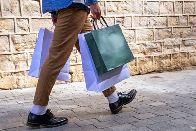 Crop unrecognizable man in trendy apparel with eco friendly bag walking on pavement near rough wall