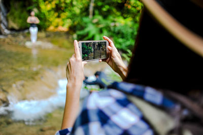 Cropped image of woman photographing through smart phone in forest