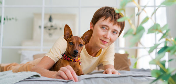 Mature woman lies on floor with slittle dog miniature pinscher