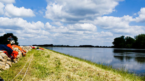 Scenic view of lake by grassy field against cloudy sky