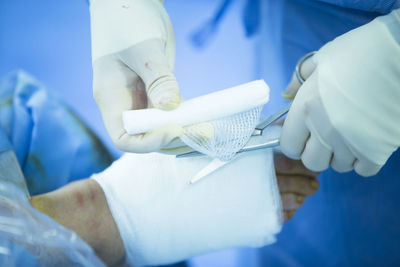 Midsection of doctor applying bandage of injured patient leg in hospital