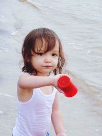 Portrait of cute girl holding red cup while standing at beach