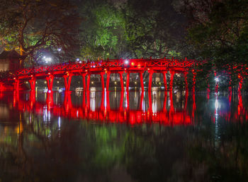 Red bridge over river against trees at night