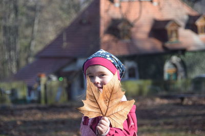 Portrait of cute girl holding maple leaf in city during autumn