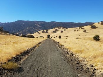 Dirt road leading towards mountains against clear blue sky