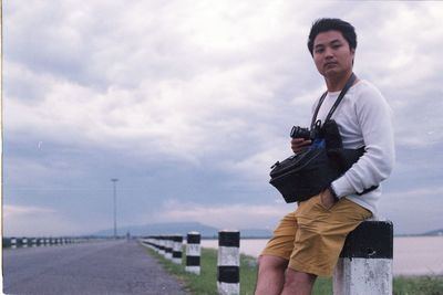 Portrait of man sitting on bollard against sky