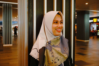 Smiling woman in headscarf standing against wall