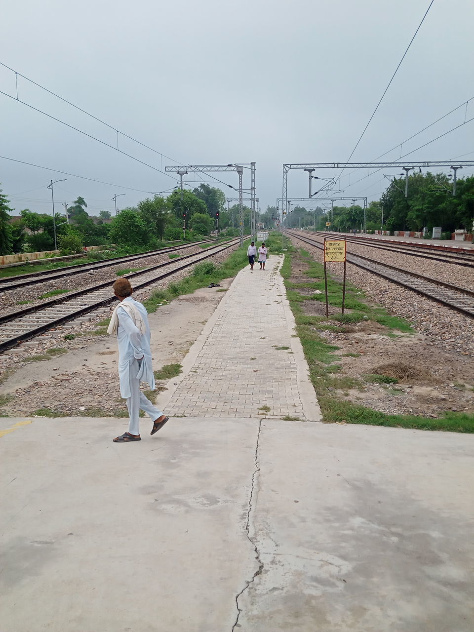 REAR VIEW OF MAN WALKING ON RAILROAD TRACKS