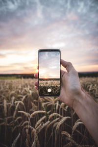 Man photographing through smart phone against sunset sky