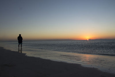 Silhouette person walking on beach against clear sky during sunset