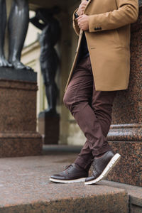 Unrecognizable handsome man in elegant autumn beige coat, brown pants and dark leather shoes