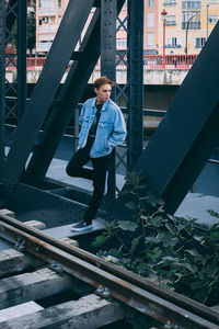 Full length of young man standing on bridge by railroad track