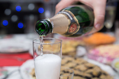 Close-up of hand pouring drink in champagne flute at table