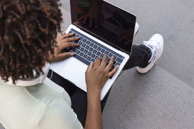 College student sitting on the stairs working on a laptop.