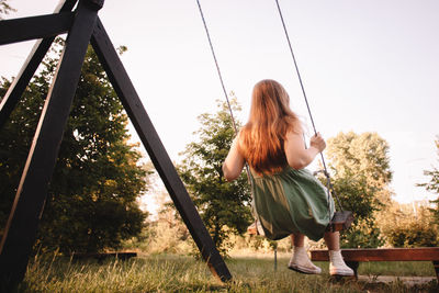 Teenage girl swinging in park during summer