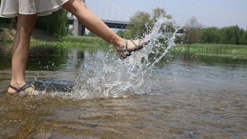Low section of woman splashing water in lake