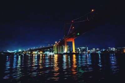 Illuminated bridge over river by buildings against sky at night