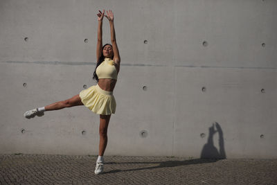 Full length of young woman jumping against wall