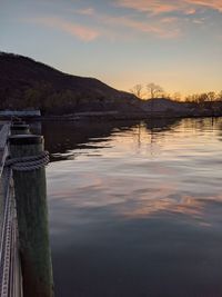 Wooden posts in lake against sky at sunset