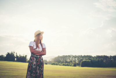 Woman wearing hat and casuals standing on field against sky