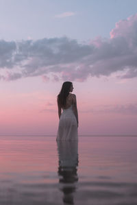 Rear view of woman standing against sea during sunset