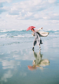 Side view of woman holding umbrella at beach against sky